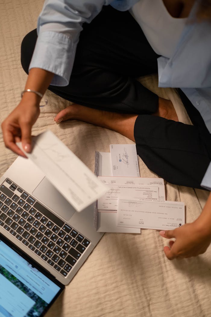services-01 An adult organizing cheques and using a laptop indoors for financial tasks.